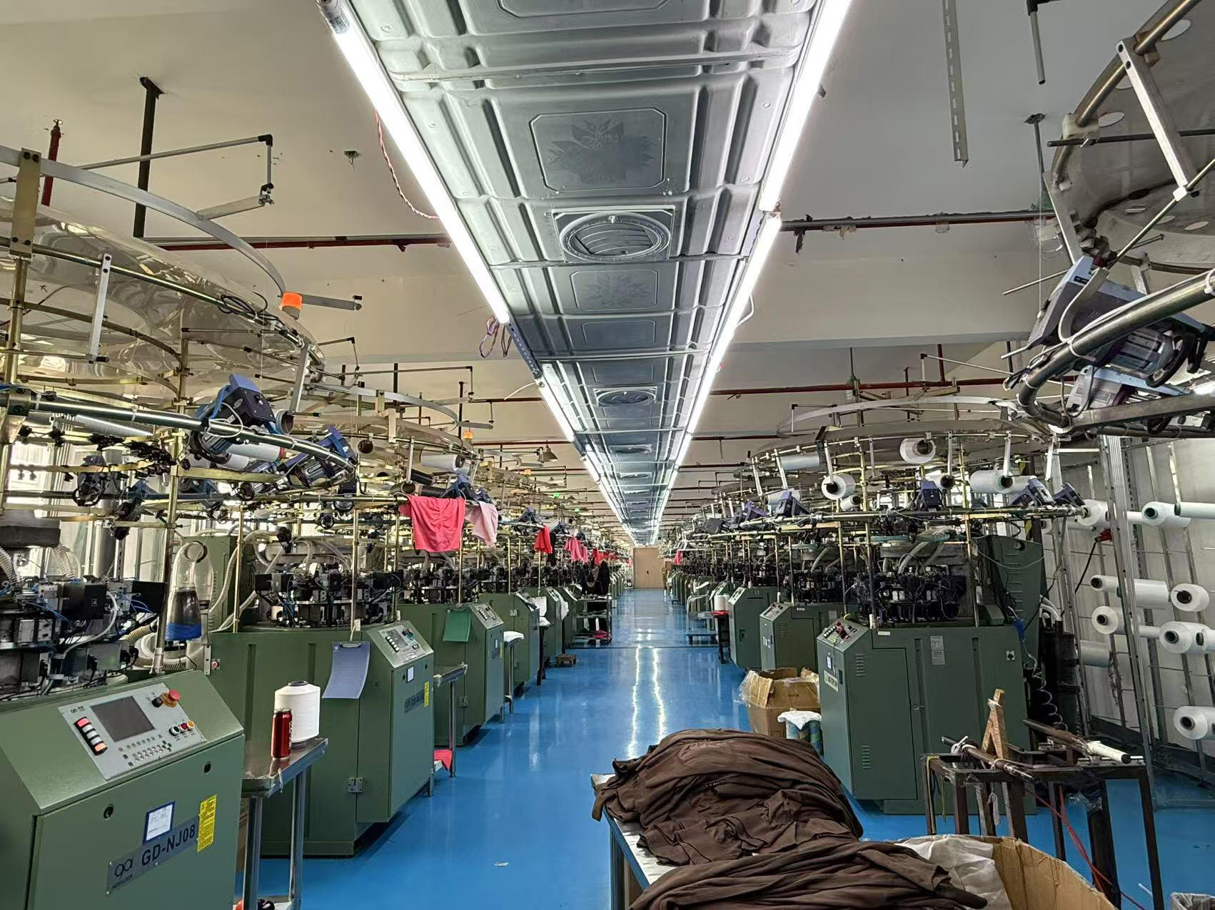 Rows of circular knitting machines beside a blue aisle in the Yiwu workshop